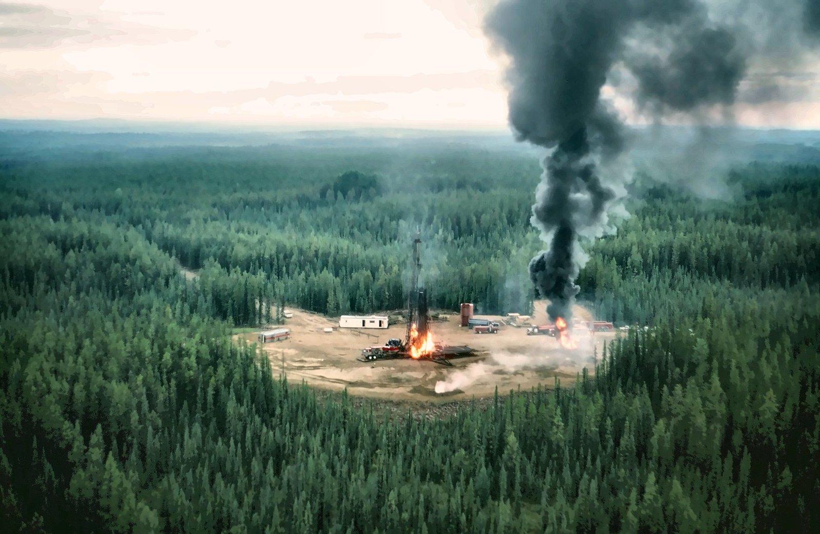 Aerial view of the burning gas well site surrounded by boreal forest, with black smoke rising